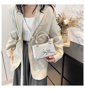 Detail of silver metallic mini bag featuring heart cutout and bow detail on beige blazer