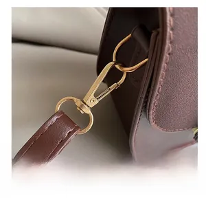 Detail shot of the golden metal hook and stitching on dark brown leather saddle bag