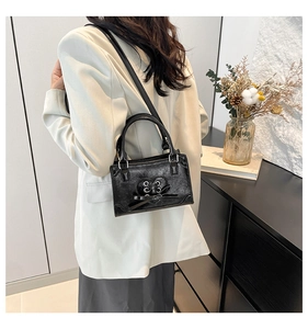 Detail of black glossy leather crossbody bag featuring heart-shaped silver eyelet lacing