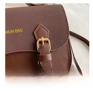 Detail showing the brown crossbody bag's gold metal buckle and pebbled leather texture