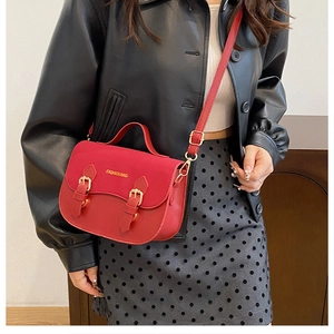Detail of red vintage saddle bag with gold hardware and fashion bag logo on flap