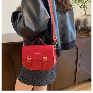 Detail view of red saddle handbag with gold buckles and adjustable shoulder strap