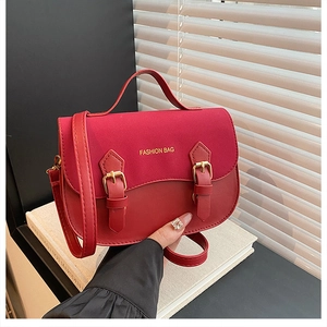 Detail of red textured crossbody bag with mixed leather finish and metal buckle hardware