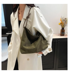 Detail of olive green suede tote bag with knotted strap on a white trench coat