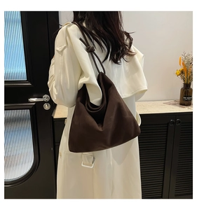 Detail shot of a dark brown suede tote bag with a unique knot design on the shoulder strap