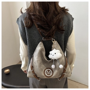 Detail of vintage brown textured backpack with M logo and plush cloud charm accessory