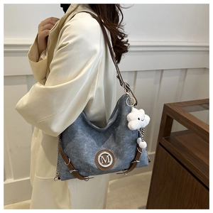 Detail view of large grey denim hobo bag with white M logo and plush cloud charm