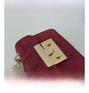 Detailed close-up of a burgundy suede crossbody bag with premium gold metallic lock buckle