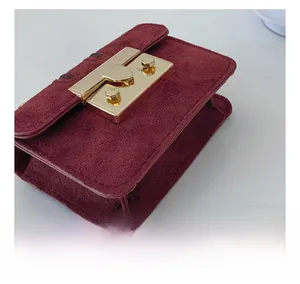 Detailed close-up of burgundy suede mini crossbody bag with golden push-lock hardware