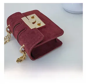 Detail of burgundy suede mini crossbody bag with golden chain and push-lock buckle