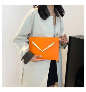 Detail of a bright orange envelope clutch featuring a V-shaped gold metal trim design