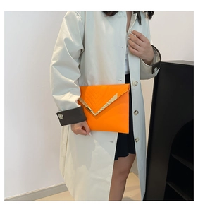 Detail of orange envelope clutch featuring golden V-metal trim and V-shaped quilted texture
