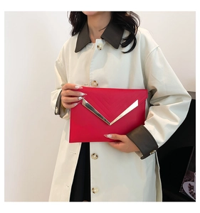 Detail of red envelope clutch with V-shaped metal trim held by a model in a trench coat