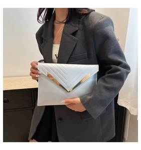 Detail of silver envelope clutch bag with gold V-trim held by a model in a gray suit