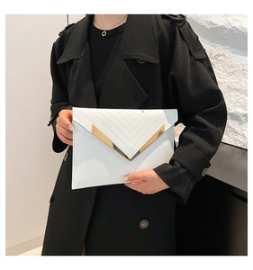 Detail of white envelope clutch featuring V-shaped quilted stitching and gold metal trim