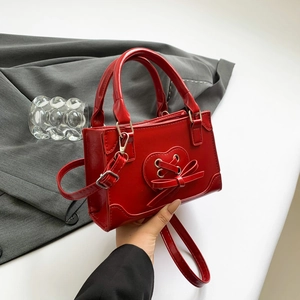 Borsa a tracolla rossa lucida con fiocco e cuore mostrata su sfondo di abito grigio