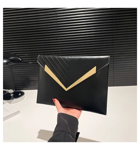 Detail of black envelope clutch featuring gold V-shaped metal trim and chevron stitching