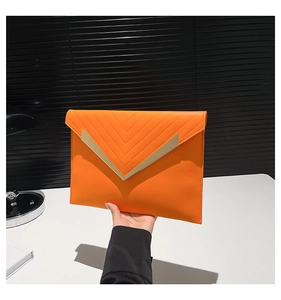 Close-up of bright orange envelope clutch with V-shaped gold trim and quilted leather detail