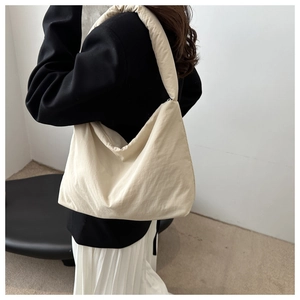 Détail d'un sac hobo en nylon crème porté par un mannequin dans un décor épuré
