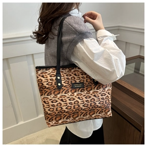 Close-up of leopard print tote bag with black shoulder straps and brand patch detail
