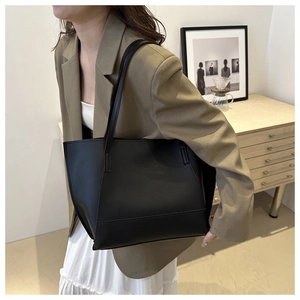 Minimalist black leather tote bag worn by a model in a stylish workplace setting