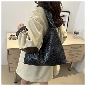 Dettaglio di una borsa tote nera intrecciata con trama in pelle lucida e tracolla alla moda