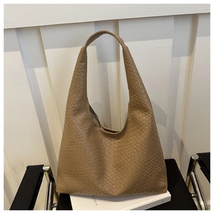 Detail of khaki hobo bag with embossed weave texture on a white book and chair
