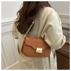 Details einer braunen Schultertasche mit Krokoprägung, Goldverschluss und Kette