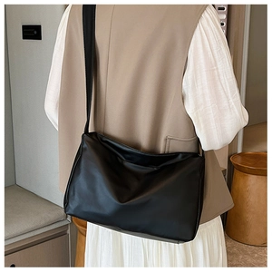 Close-up of a large black faux leather shoulder bag worn on a beige blazer for daily commute