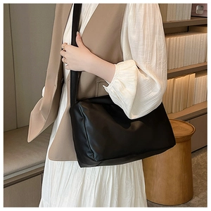 Detail of soft black PU leather crossbody bag worn with a white pleated dress