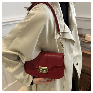 Detail der weinroten Kroko-Umhängetasche mit Goldkette auf einem beigen Trenchcoat