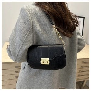 Close-up of black crocodile pattern saddle bag with gold buckle on grey wool coat