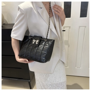 Detail of black quilted tote bag with silver bow accent and classic chain strap
