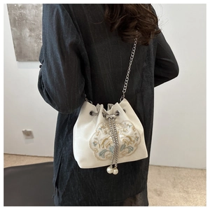 Detail of cream drawstring bucket bag featuring floral embroidery and pearl accents