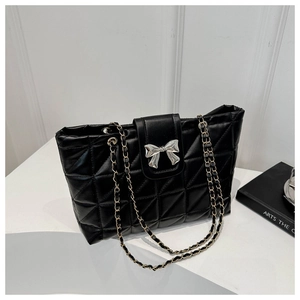 Detail of black quilted tote bag with silver bow clasp and woven chain strap