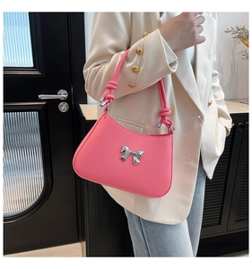 Détail du sac à bandoulière rose avec nœud argenté porté en travers du corps par un mannequin