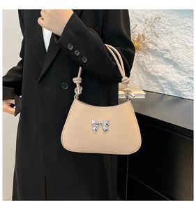 Détail d'un sac demi-lune beige avec noeud métallique argenté et doubles bretelles nouées