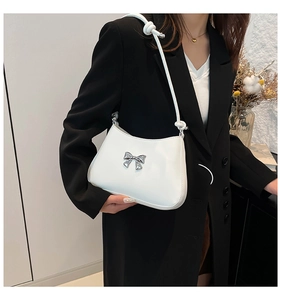 Détail d'un sac bandoulière demi-lune blanc avec nœud argenté sur un blazer noir
