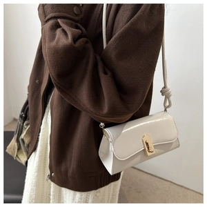 Detail of a beige PU leather crossbody bag with a golden twist lock and knotted strap