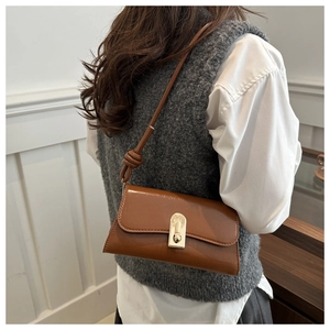 Close-up of brown textured baguette bag with gold twist lock and knot detail on strap