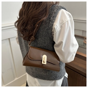 Detail of dark brown patent leather baguette bag with a gold metal clasp and knotted strap