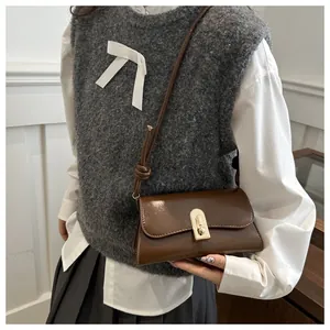 Detailed close-up of brown vintage handbag with gold clasp worn with grey sweater