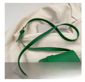 Detail of adjustable strap with gold buckle on green crossbody bag over white blazer