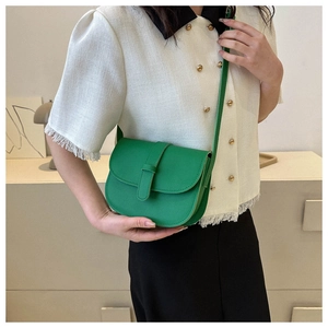 Vibrant green saddle crossbody bag styled with a white tassel shirt and black skirt