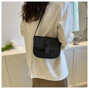 Minimalist black faux leather crossbody bag shown on a model in a cozy home setting
