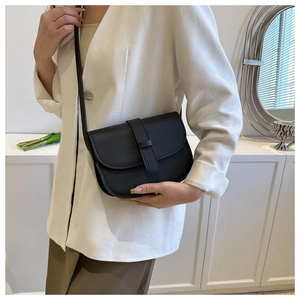 Model wearing a black saddle crossbody bag in faux leather with flap closure and slim strap