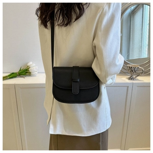 Detail view of a black minimalist saddle crossbody bag worn over a white blazer jacket