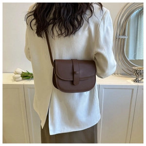 Detail view of a dark brown saddle bag with a leather strap worn by a model in a room