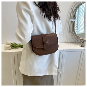 Side view of a dark brown saddle bag worn with a white blazer in a minimalist setting