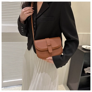 Brown matte leather saddle bag worn cross-body style over a black blazer and white skirt